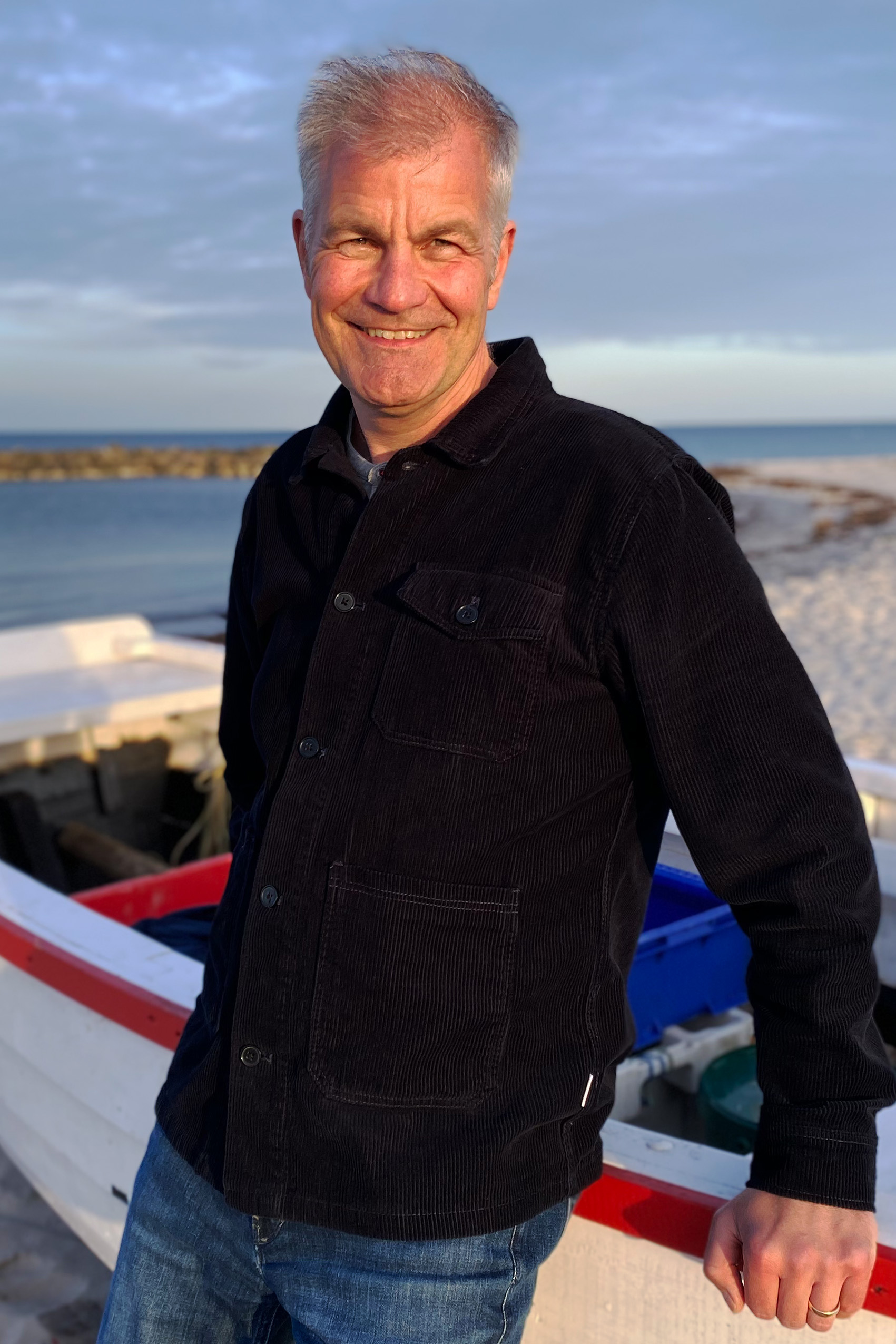 Volkert Brammer am Ostseestrand, lehnt sich an Boot und lächelt in die Kamera